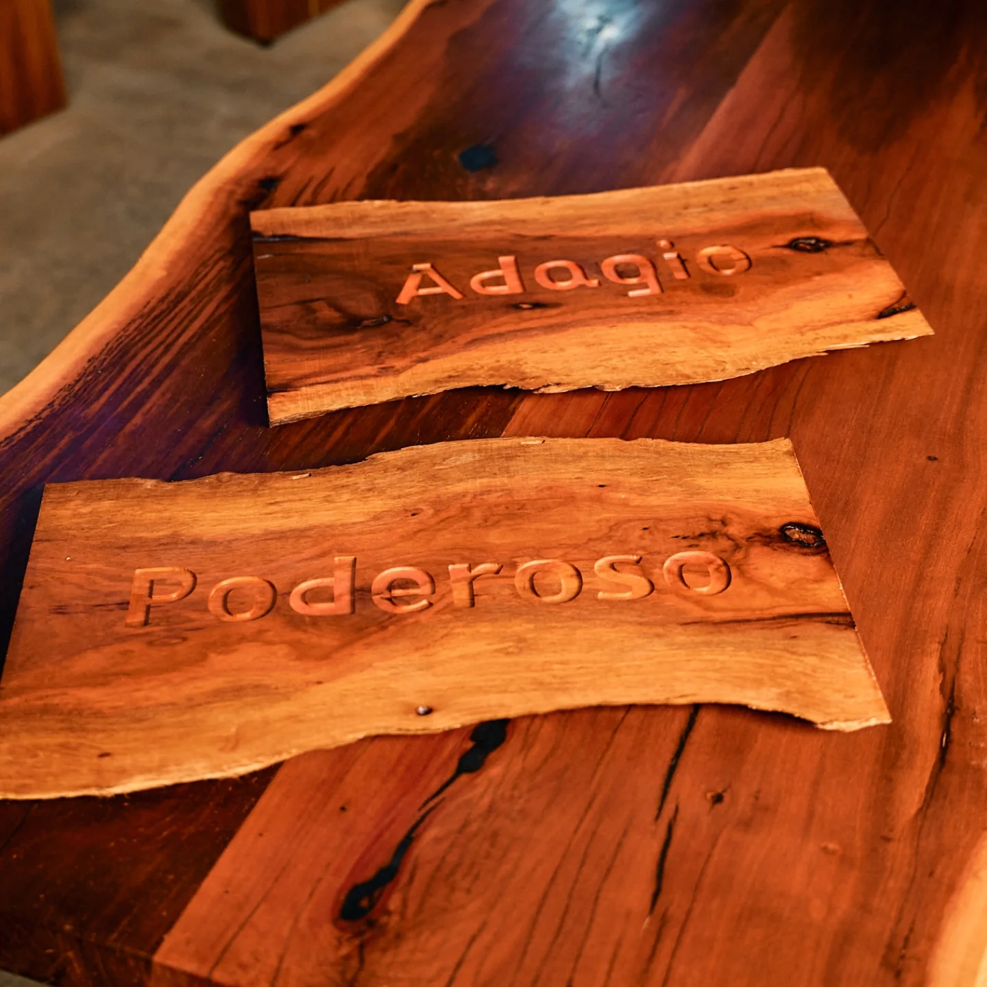 Hand-carved wood nameplates reading Adagio and Poderoso on a live-edge tabletop