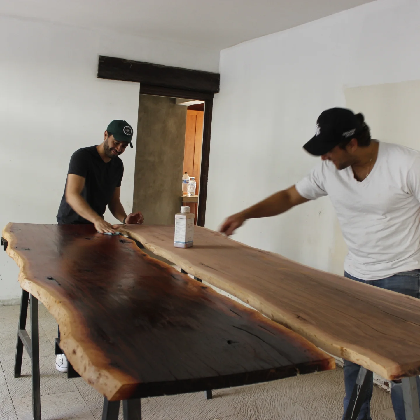 Two Madera Selva craftsmen hand-finishing a live-edge slab in the San Diego workshop